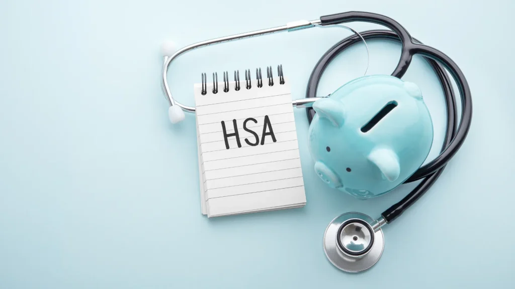 HSA written on a lined notepad next to a blue piggy bank and stethoscope