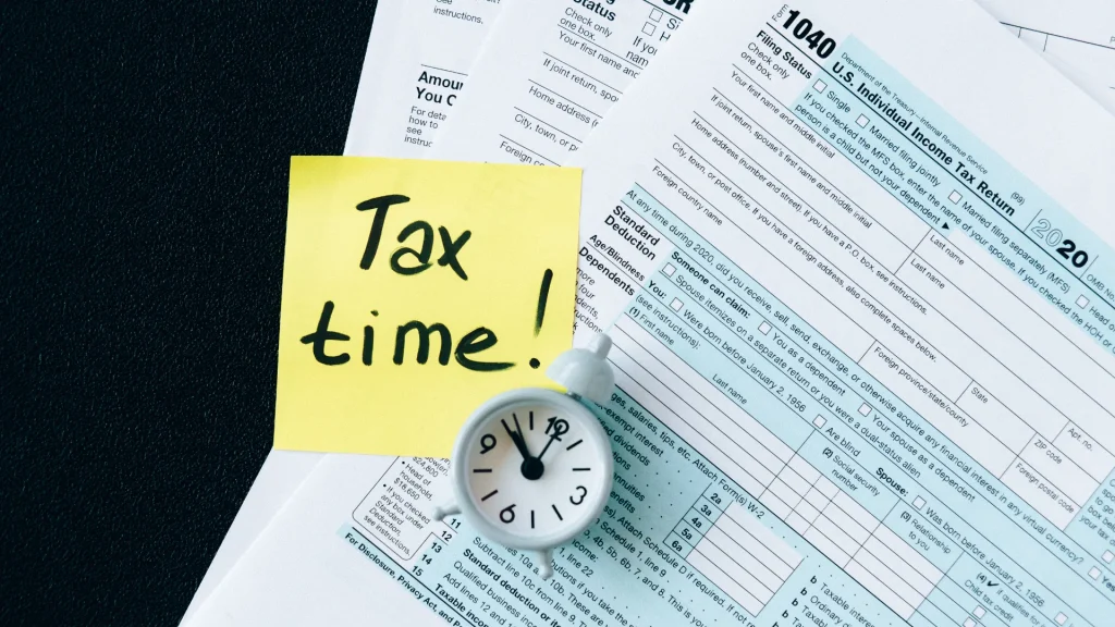 Tax documents with a yellow post-it note that says "Tax Time!" with a small alarm clock